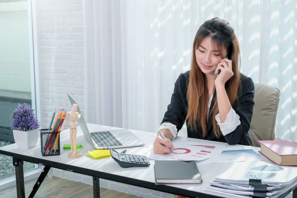 Attractive young asian woman talking on the mobile phone at her working place in office.